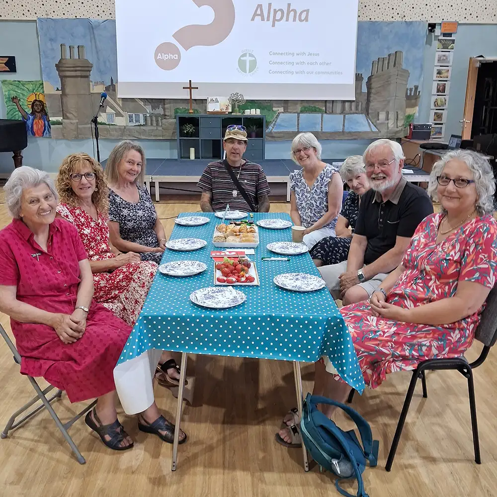 People gathered together around a table before sharing food at Alpha